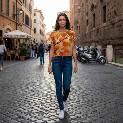 Woman walking on a European cobblestone street wearing a cropped tee with an all over print of golden autumn leaves in amber and sienna tones, botanical branch pattern across the chest, natural city lifestyle scene, realistic fabric drape and fit in daylight