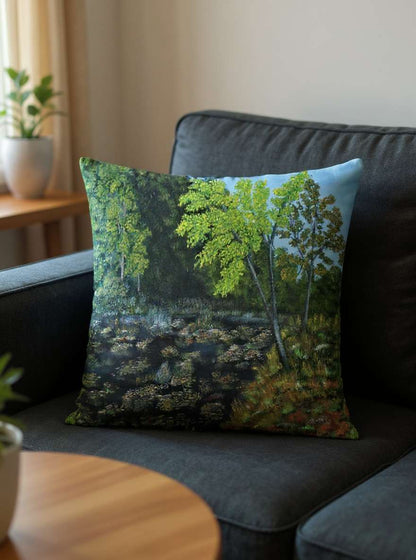 All-Over Print Basic Pillow on a dark sofa, featuring the Pond design with green summer trees, water reflections, and lush foliage. Soft indoor light highlights the peaceful atmosphere and natural colors.