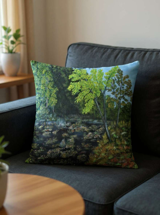 All-Over Print Basic Pillow on a dark sofa, featuring the Pond design with green summer trees, water reflections, and lush foliage. Soft indoor light highlights the peaceful atmosphere and natural colors.