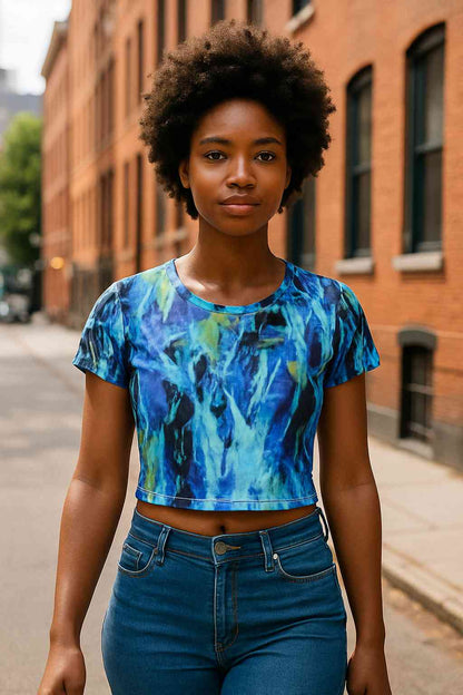 Black woman walking on a quiet urban street wearing a blue and green all over print crop tee with impressionist abstract nature pattern fluid brush textures denim jeans summer daylight lifestyle modern streetwear confident posture calm creative atmosphere