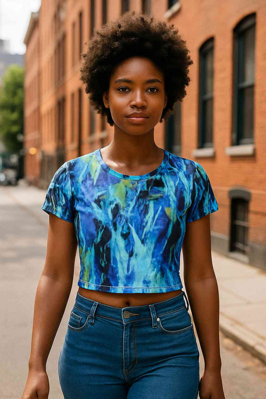 Black woman walking on a quiet urban street wearing a blue and green all over print crop tee with impressionist abstract nature pattern fluid brush textures denim jeans summer daylight lifestyle modern streetwear confident posture calm creative atmosphere