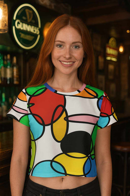 Red haired woman smiling in an Irish pub wearing a colorful geometric circle chain all over print crop tee inspired by 60s 70s retro design vibrant red yellow turquoise and green shapes casual chic streetwear look warm indoor light social lifestyle scene with natural posture confident attitude modern urban bar atmosphere