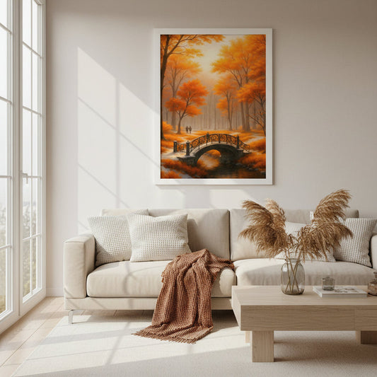 Framed poster Golden Autumn Bridge hanging above a beige sofa in a bright modern living room with large windows, soft natural daylight and light wood furniture, showing an autumn forest landscape with glowing orange trees, a curved bridge over water and two distant walkers