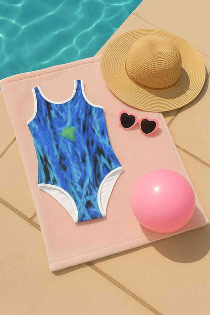 Kids swimsuit with impressionist blue design showing tall grass and flowers in soft natural tones, artistic summer style flat lay beside pool, creative modern swimwear for children