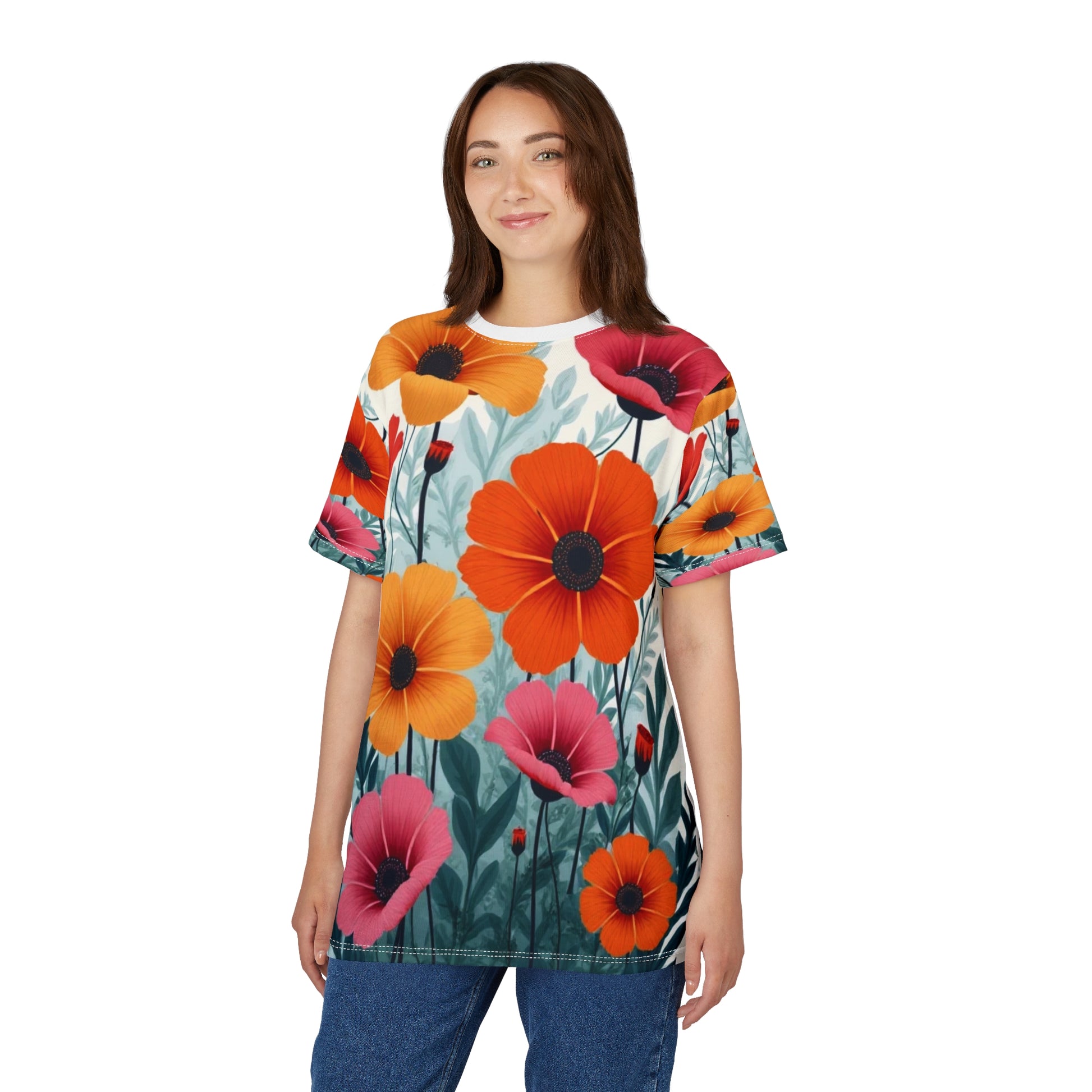 Unisex AOP Cut & Sew Tee with a retro floral design featuring oversized orange, pink, and red 60s-inspired blooms, modeled by a woman standing in casual jeans, bright vintage festival fashion look.