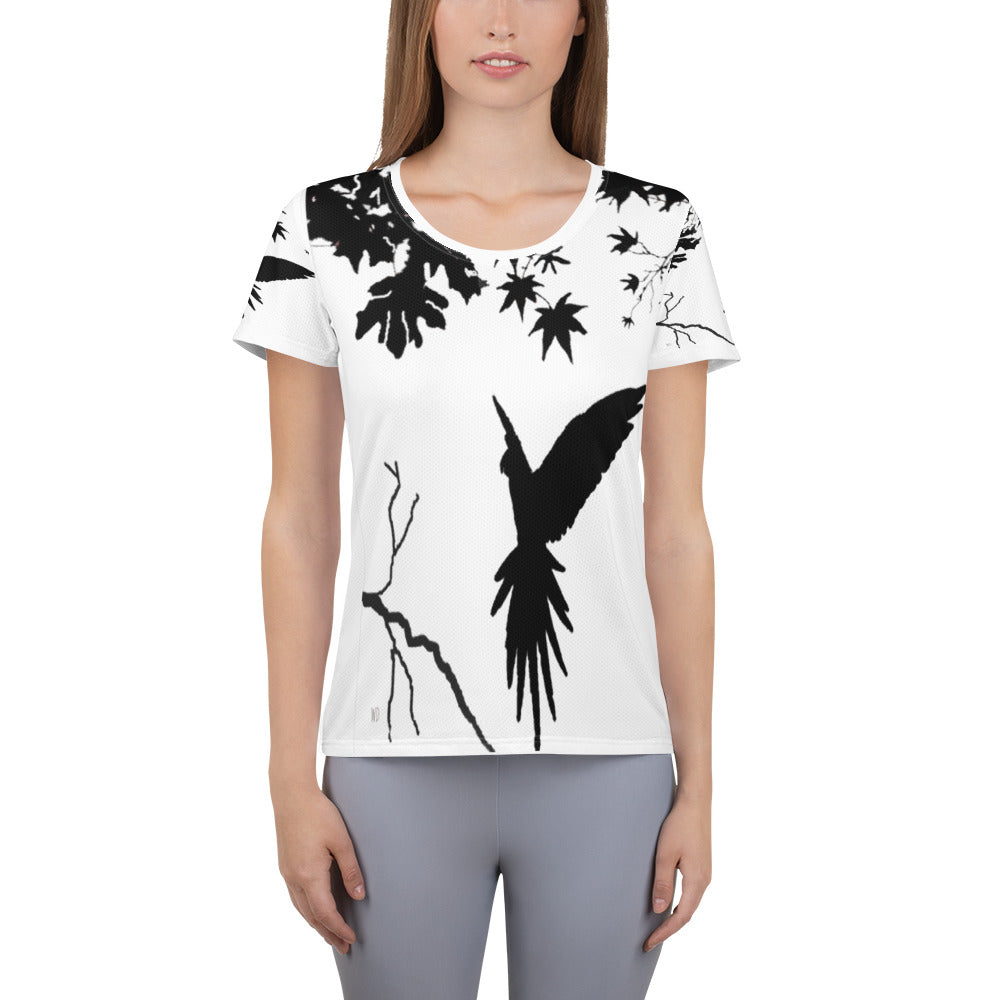 Women’s athletic t-shirt with black silhouette of a parrot in flight, landing on a tree branch, surrounded by bare branches and scattered leaves on a light background.
