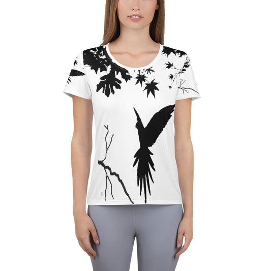 Women’s athletic t-shirt with black silhouette of a parrot in flight, landing on a tree branch, surrounded by bare branches and scattered leaves on a light background.